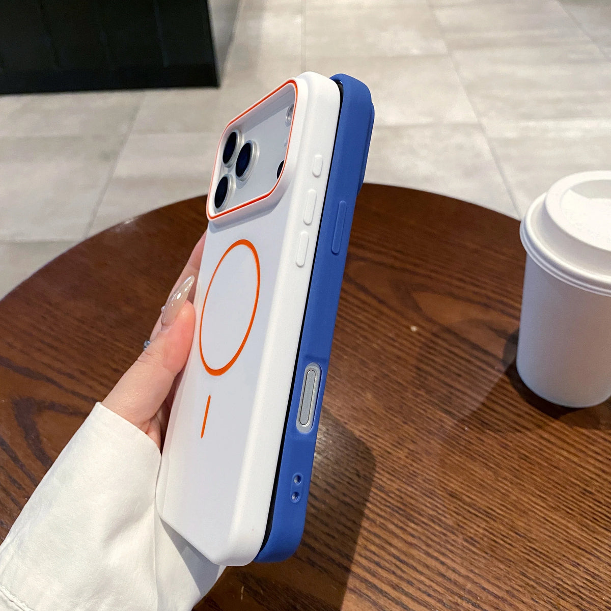 A hand holds a white and blue Magnetic Matte phone case with MagSafe support on a wooden table.
