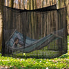 A large mesh fly net canopy is suspended, featuring a hammock-like structure with a person relaxing inside in a wooded outdoo
