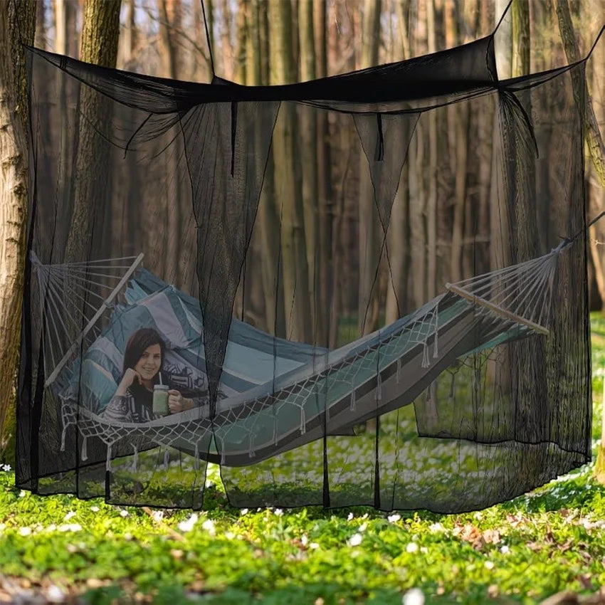 A large mesh fly net canopy is suspended, featuring a hammock-like structure with a person relaxing inside in a wooded outdoo