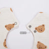 A close-up view of a light beige muslin cotton baby bib with a brown bear design and an adjustable snap closure.