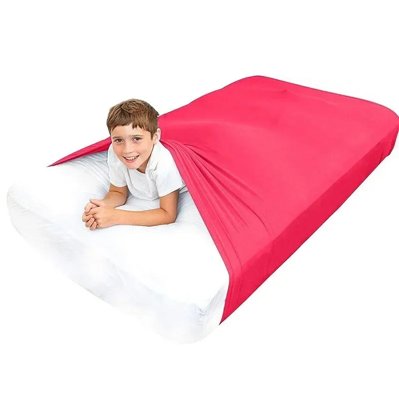 A smiling boy lying on a white bed sheet covered by a bright pink breathable stretchy sensory sheet.