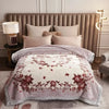 A beige weighted plush blanket with a floral pattern is displayed on a bed in a light-colored room.