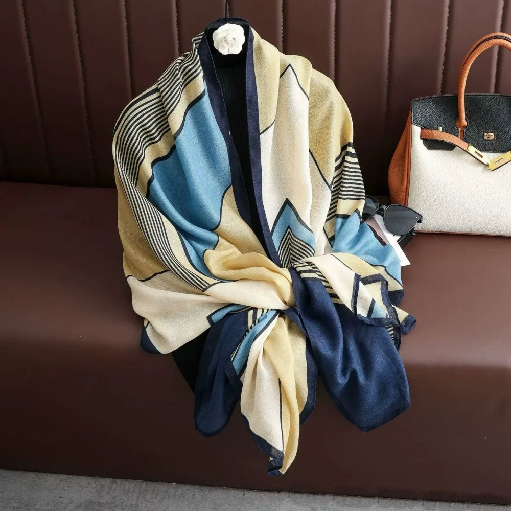 A large color-block scarf and shawl featuring shades of blue, beige, and navy fabric draped on a brown surface.