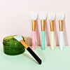A collection of silicone facial mask brushes with gold and colored handles displayed on a light surface.