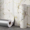 Roll of gold foil marble peel-and-stick wallpaper displayed against a white marble background.