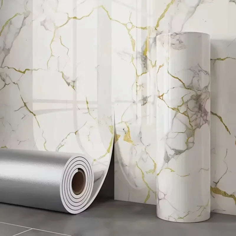 Roll of gold foil marble peel-and-stick wallpaper displayed against a white marble background.