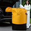 A woman holds a large yellow waterproof storage bag filled with white pillows next to a car trunk.
