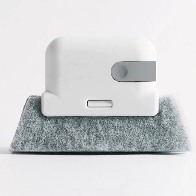 A white multi-surface gap cleaning brush with a silver pad resting on a gray felt surface.