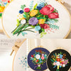 A close-up of a floral cross stitch embroidery kit showing various colored fabric flowers and greenery on white linen.