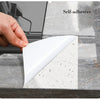 A hand peels a white self-adhesive marble pattern sheet from a gray marble surface.