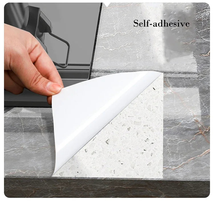 A hand peels a white self-adhesive marble pattern sheet from a gray marble surface.