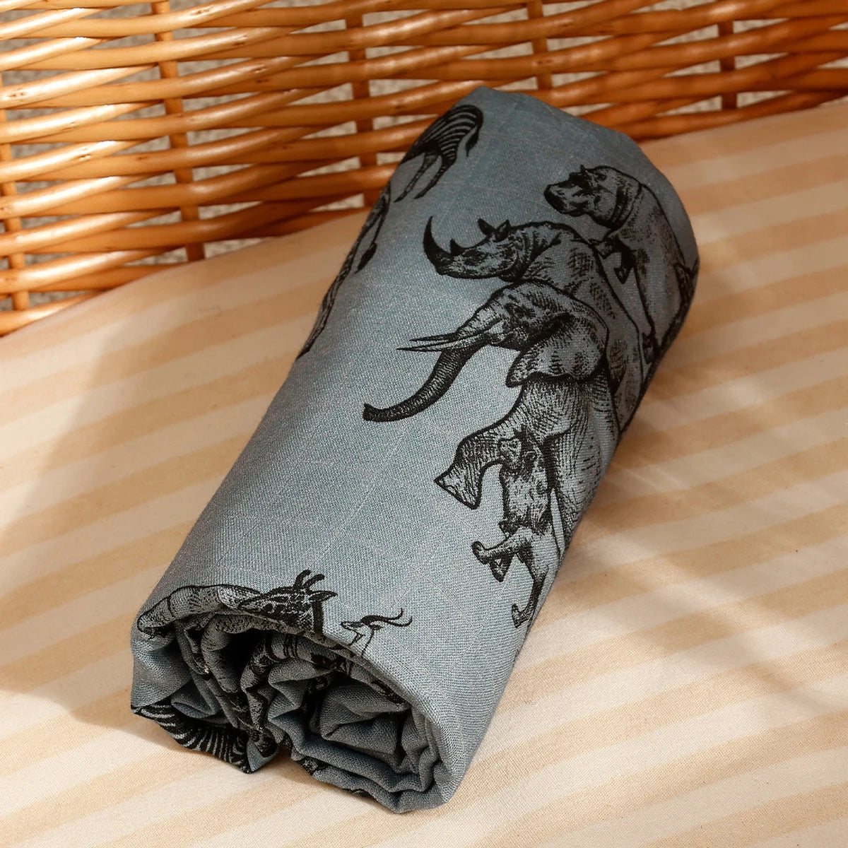 A gray muslin baby swaddle blanket featuring a black and white illustration of various animals.