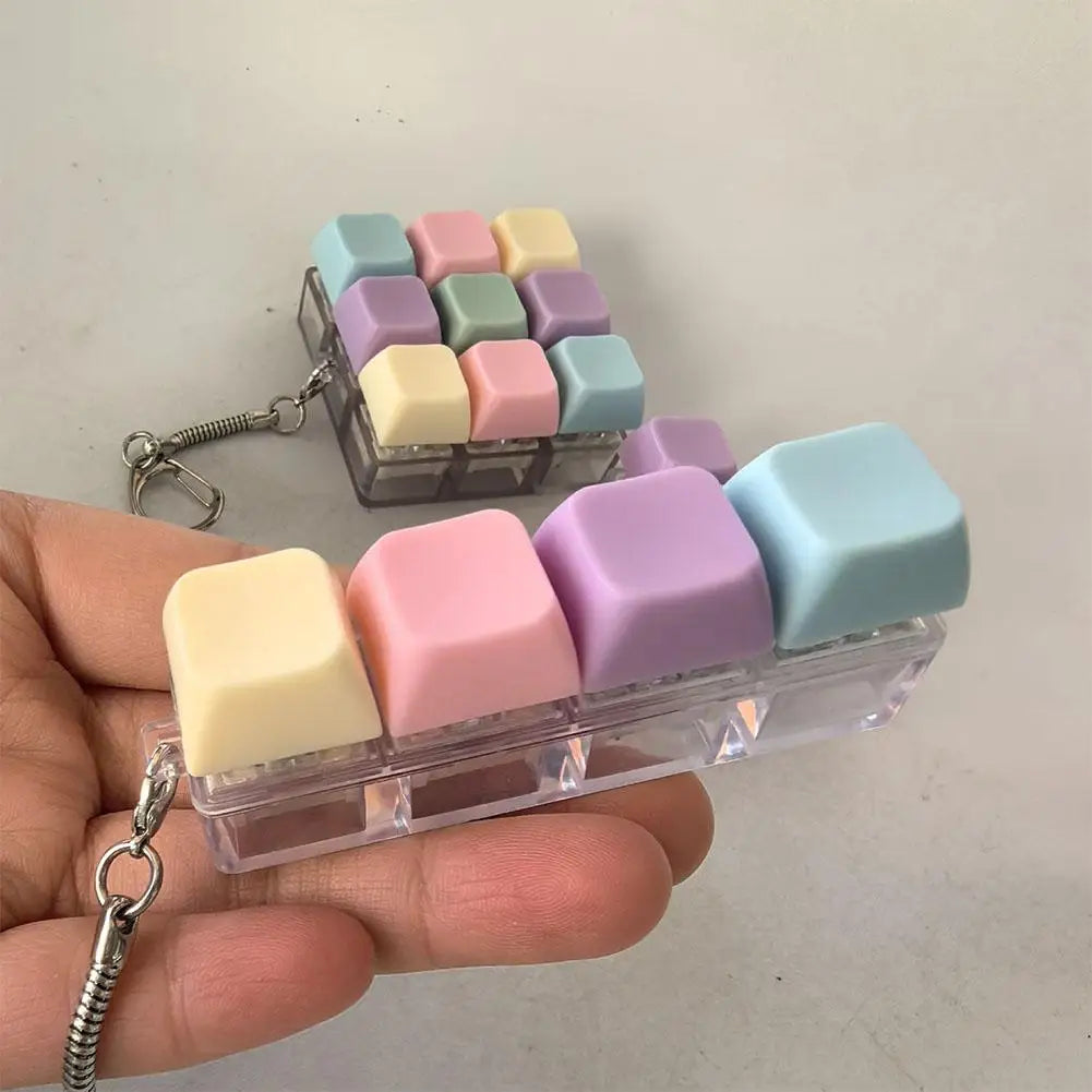 A hand holds a clear plastic keychain containing colorful mini mechanical keyboard fidget cubes for stress relief.