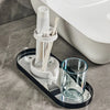 A modern bathroom toothbrush holder with a dust cover and drainage is placed on a black tray next to a toilet bowl.