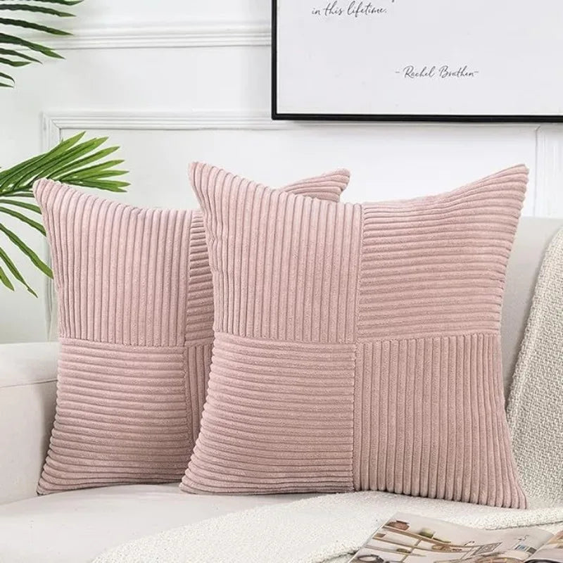 A set of two pink corduroy patchwork throw pillow covers with vertical ribbing on a white sofa.