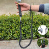 Une main tient une corde élastique réglable avec un collier métallique, devant un arrière-plan de haie verte.