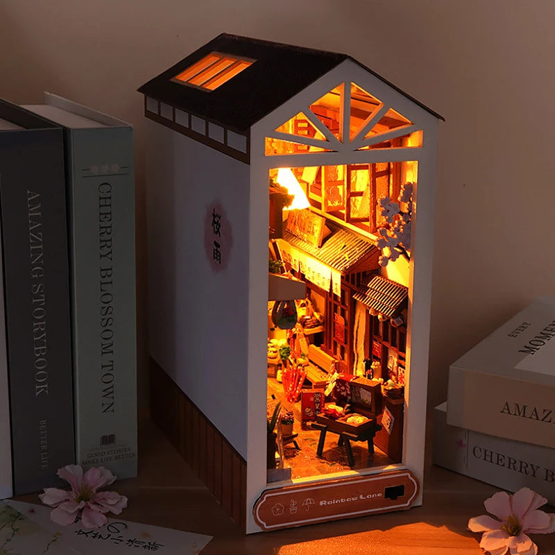 A miniature DIY book nook kit featuring a lighted wooden bookshelf room scene with an attic roof.