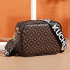 A brown patterned compact crossbody bag with black trim and white lettering is shown on a light surface.