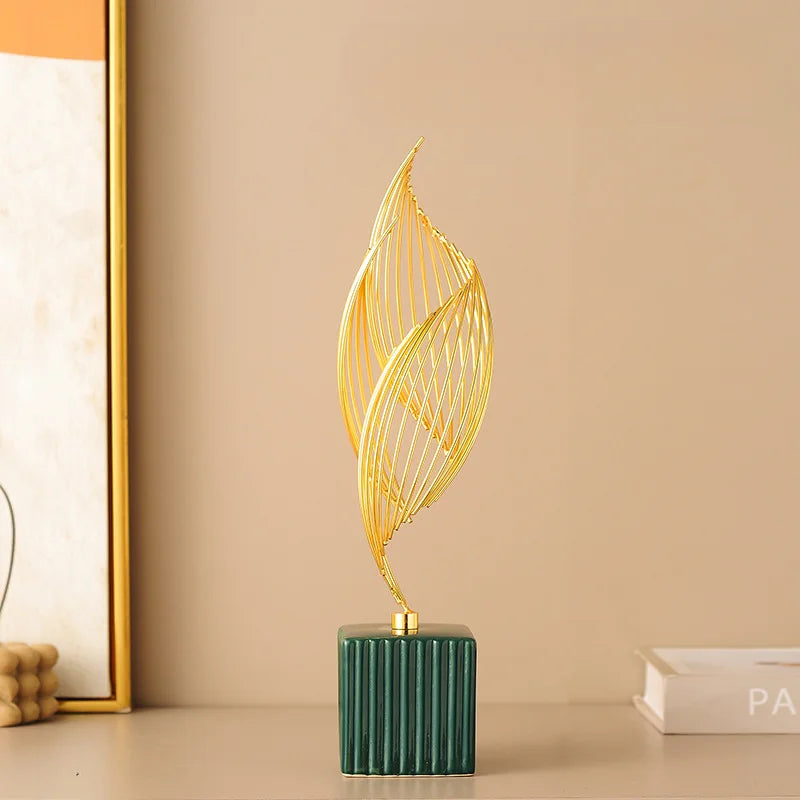 A golden, leaf-shaped sculpture stands on a dark green ceramic block against a neutral background.