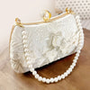 A light beige pearl embroidered evening clutch with a gold chain strap resting on a wooden surface.