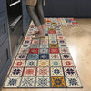 A rectangular floor mat featuring a geometric pattern in shades of blue, red, orange, and cream placed on a light wood floor.