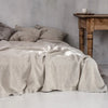 A beige linen bed sheet set with pillows is displayed on a bed in a bright, minimalist room.