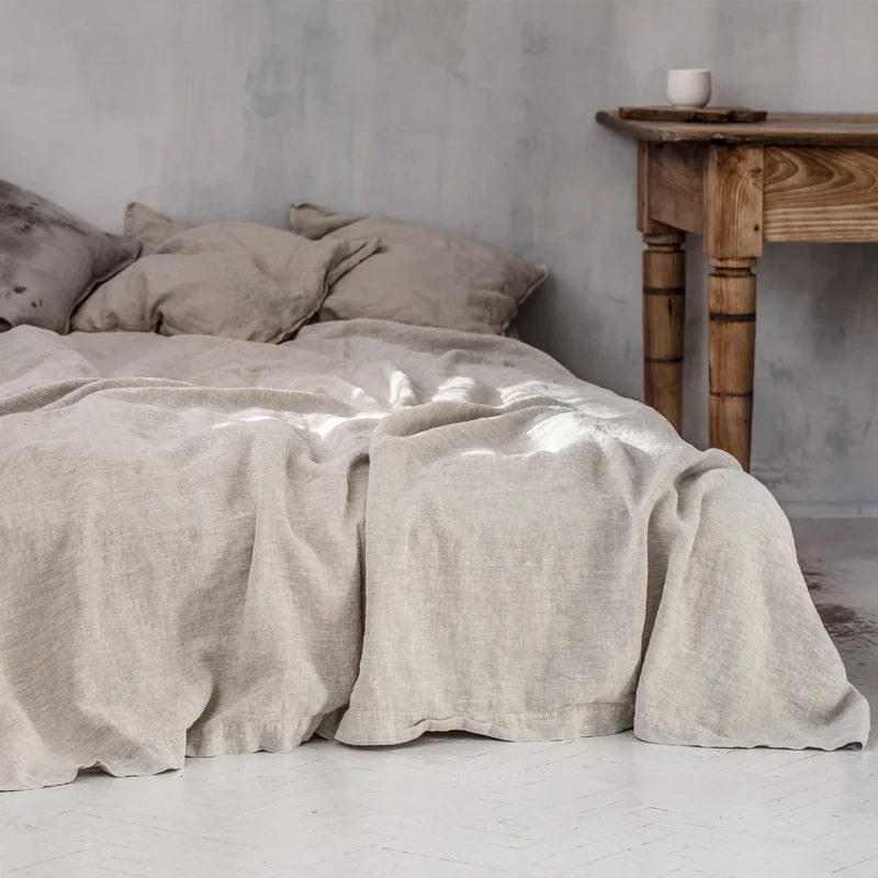 A beige linen bed sheet set with pillows is displayed on a bed in a bright, minimalist room.