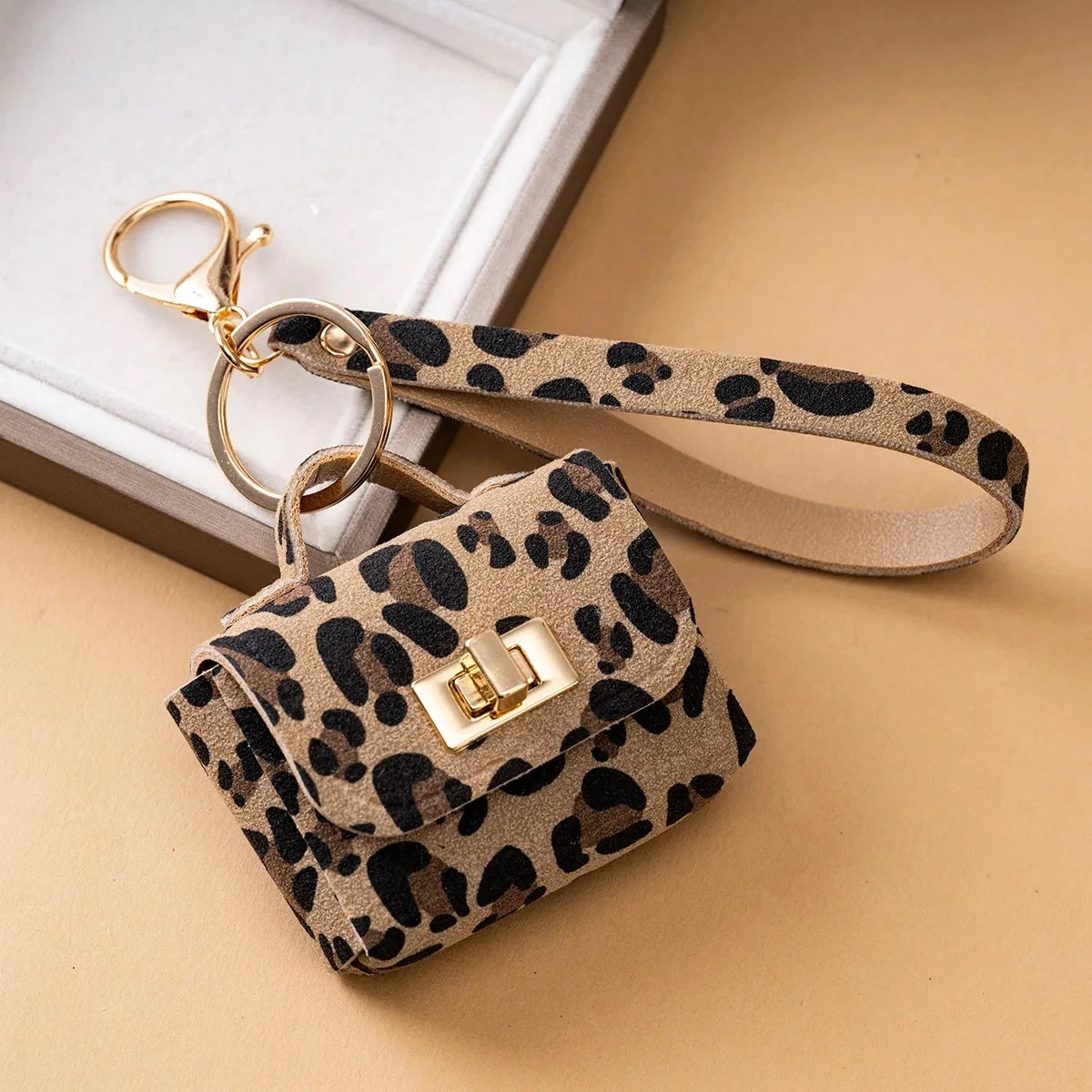 A leopard print PU leather mini wallet with a gold-toned chain attached, resting on a beige surface.