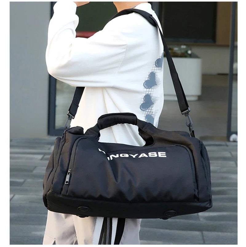 A black duffel bag with a shoe pocket is carried by a person wearing a white top.
