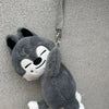 A gray and white plush toy resembling a cat or animal face is hanging by a gray strap.