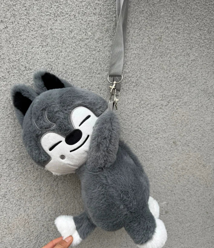 A gray and white plush toy resembling a cat or animal face is hanging by a gray strap.