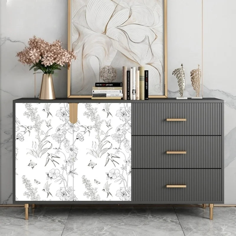A gray cabinet with a white floral peel-and-stick wallpaper panel, flanked by a framed artwork and a vase of pink flowers.
