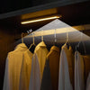 A row of light-colored clothing hangers displayed under a long illuminated shelf.