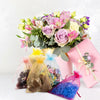 A bouquet of pink and purple flowers sits next to white organza drawstring bags for gifts and party favors.