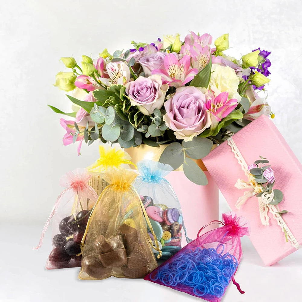 A bouquet of pink and purple flowers sits next to white organza drawstring bags for gifts and party favors.