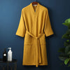 A mustard yellow lightweight cotton waffle robe hanging on a dark blue wall.