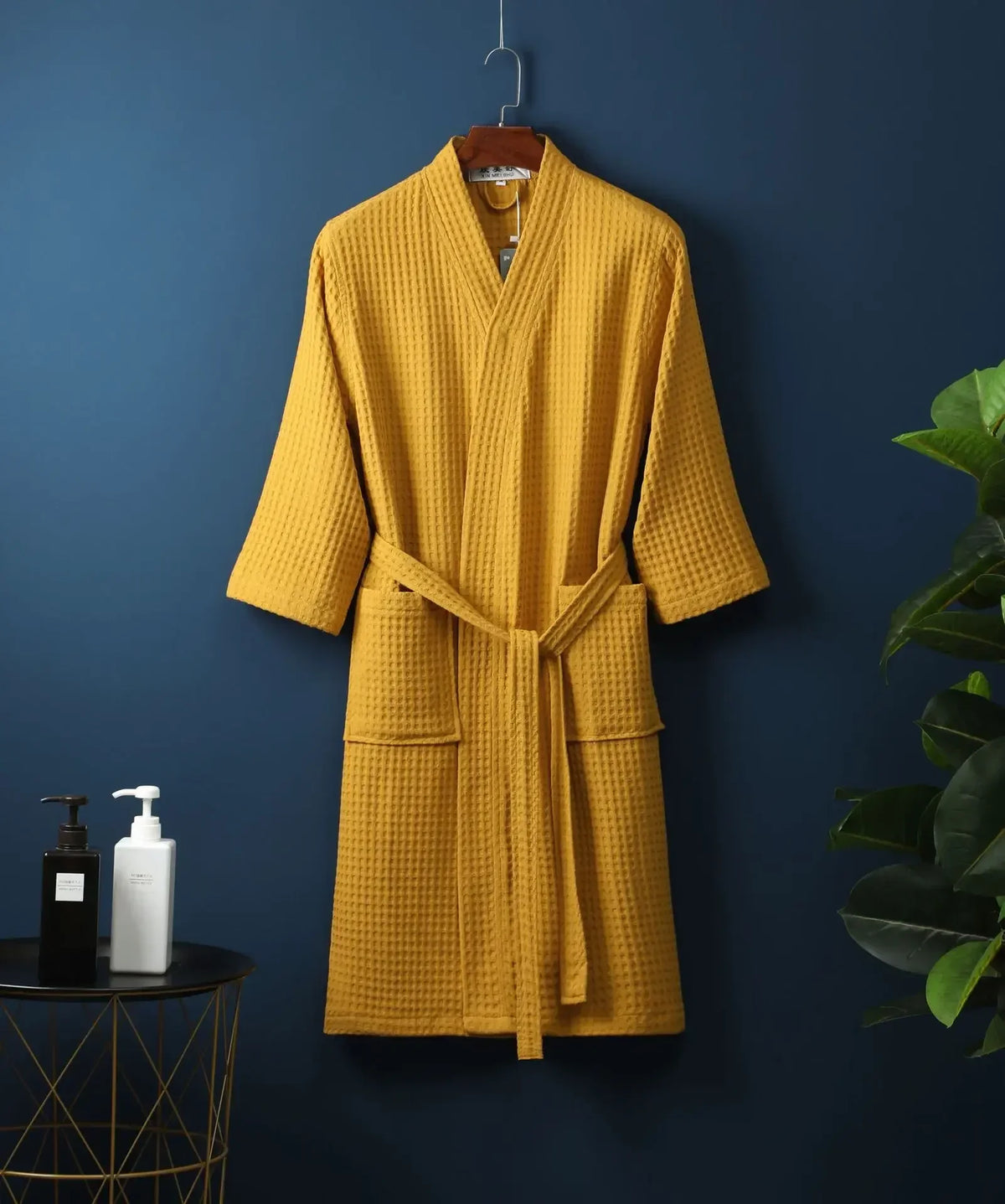 A mustard yellow lightweight cotton waffle robe hanging on a dark blue wall.