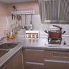 A kitchen countertop with a stainless steel sink, backsplash, and hanging utensils under a metal vent hood.