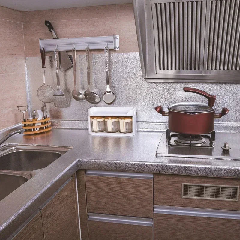 A kitchen countertop with a stainless steel sink, backsplash, and hanging utensils under a metal vent hood.