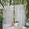 A set of two sheer white floral lace curtains hanging outdoors on a table setting.