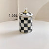 A white and black checkerboard porcelain storage jar with a gold lid sits on a white surface.