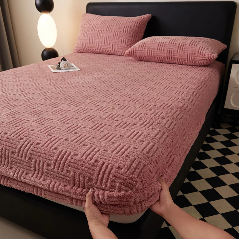 A close-up of a pink textured mattress cover with an elastic edge on a bed.