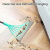 A silicone squeegee broom with a long handle is used to clean hair and trash from a wooden floor.