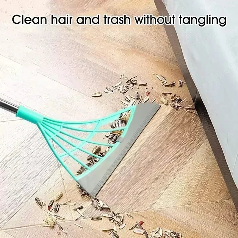 A silicone squeegee broom with a long handle is used to clean hair and trash from a wooden floor.