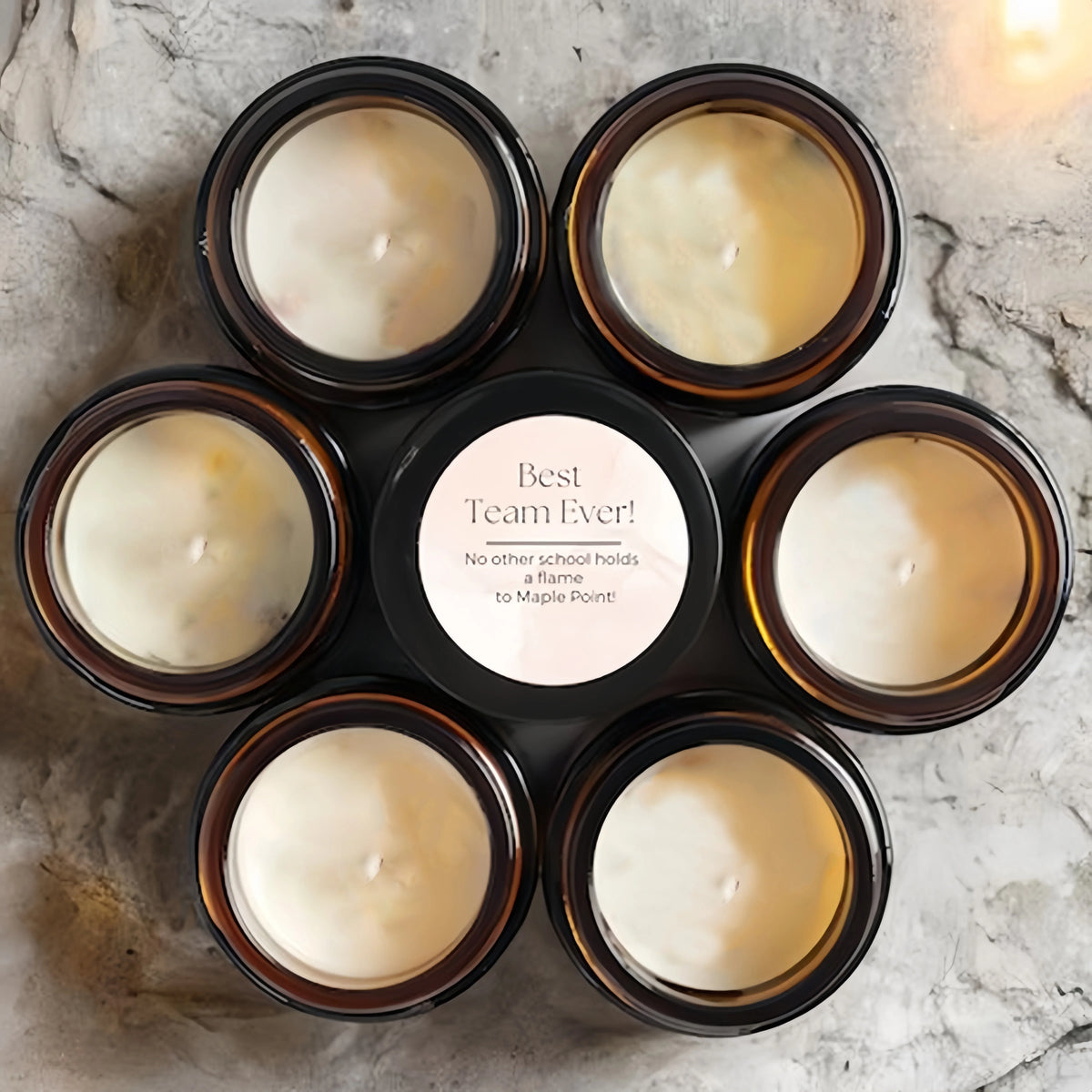 A collection of nine small glass jars filled with white scented wax candles arranged in a circular pattern.