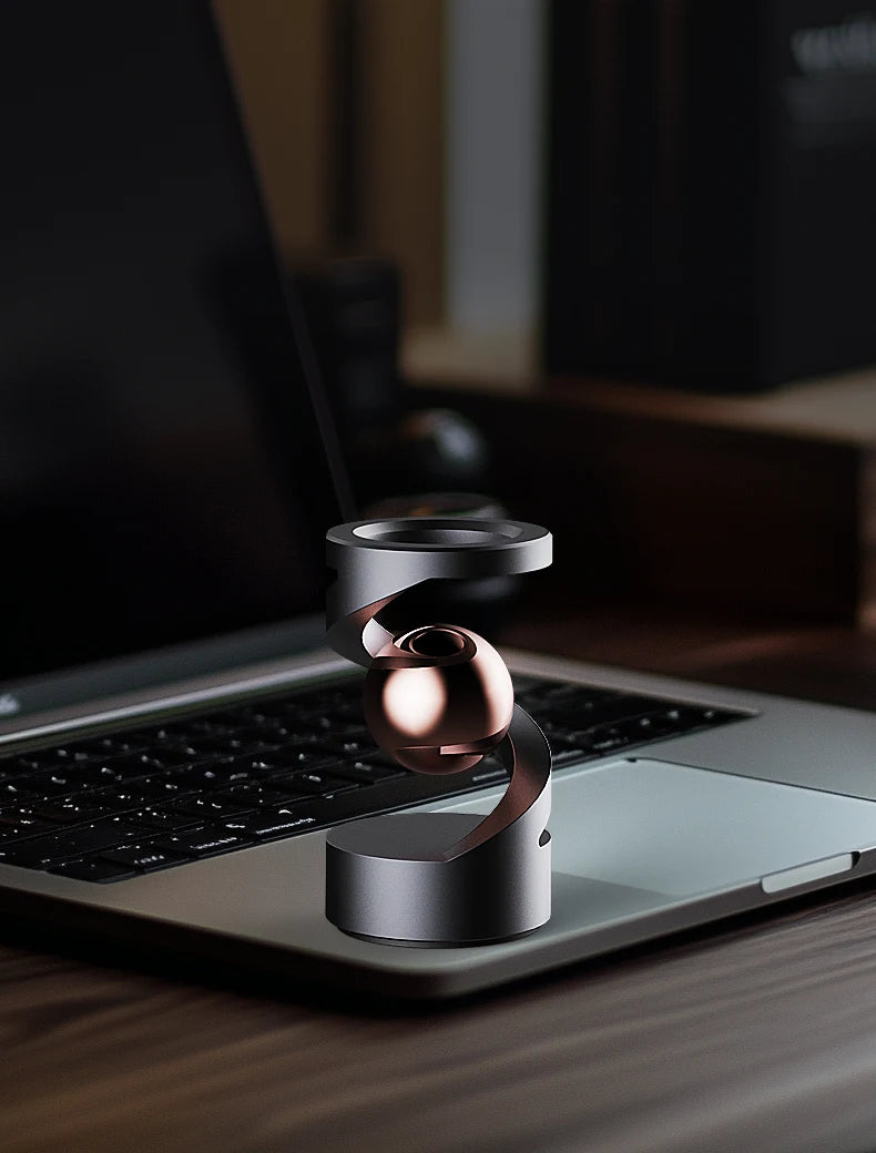 A metallic spinning top levitating above a laptop keyboard on a wooden desk.
