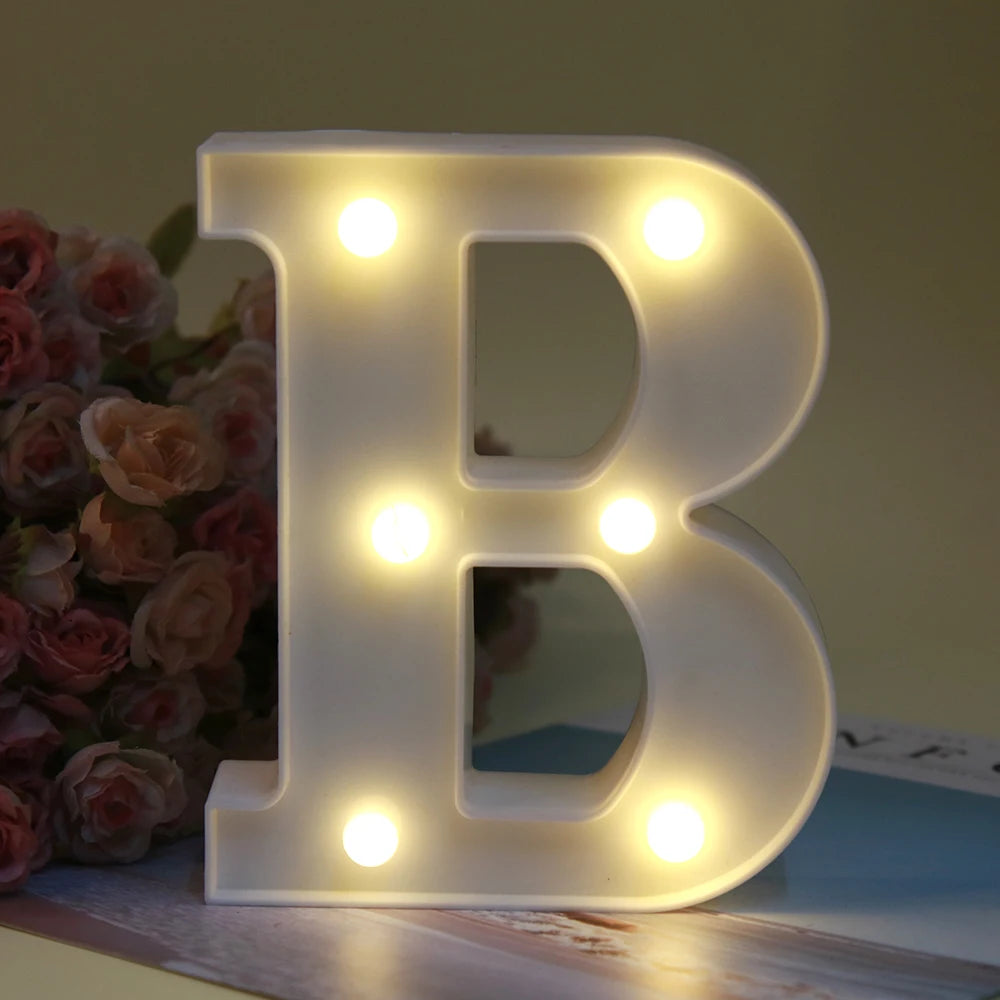 Lettre alphabet B lumineuse blanche LED, veilleuse, posée sur une surface en bois à côté de roses roses.