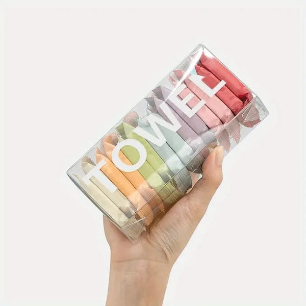Una mano sostiene un recipiente de plástico transparente lleno de toallas de viaje comprimidas de varios colores.