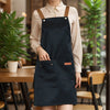 A woman wearing a dark navy polyester kitchen apron with brown straps, standing in a bright indoor setting.