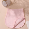 A pink, ribbed baby burp cloth is folded on a light beige surface next to a vase of dried grasses.